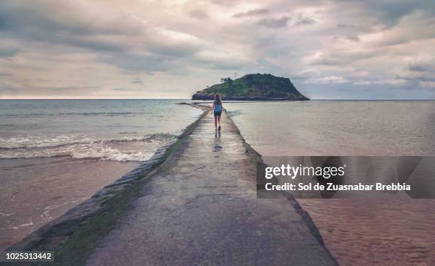 girl walking forward to land on a path surrounded by sea - comunidad autonoma del pais vasco stock-fotos und bilder