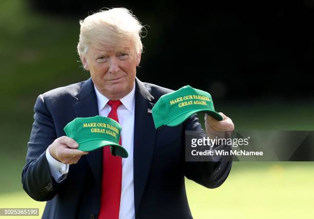 President Donald Trump holds up two hats that say "Make Our Farmers Great Again" as he departs the White House August 30, 2018 in Washington, DC....