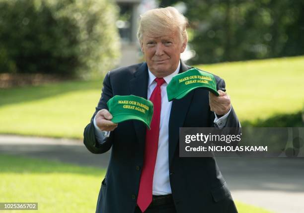 President Donald Trump displays caps reading "Make our Farmers Great Again" while walking to board Marine One as he departs the White House in...