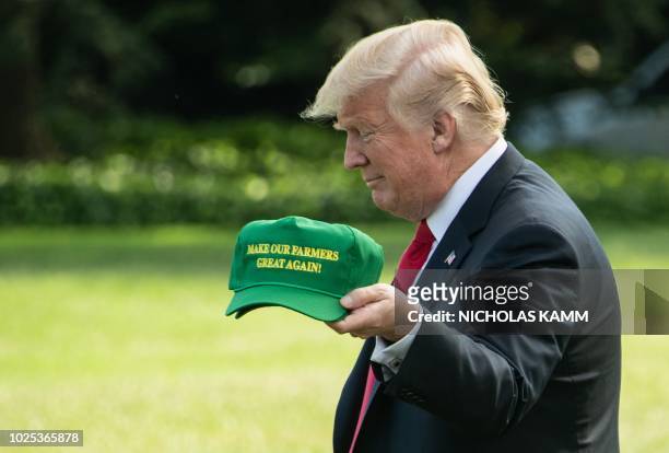 President Donald Trump displays caps reading "Make our Farmers Great Again" while walking to board Marine One as he departs the White House in...