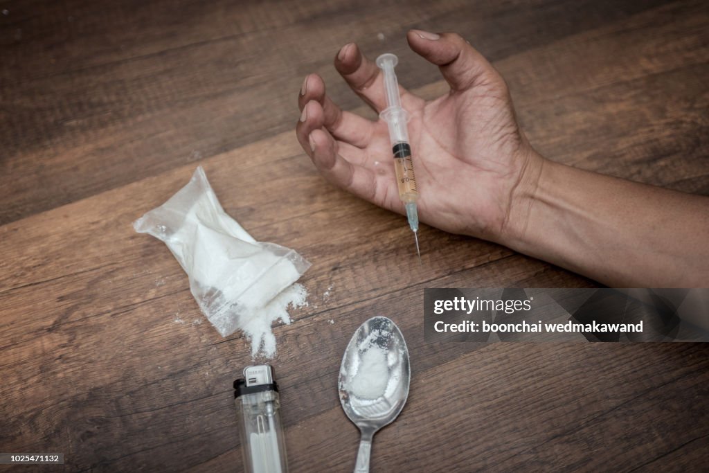 Unconscious drug addict hands lying on grungy concrete floor with pills, syringe, cooked heroine. Dangers of drug addict and abuse concept. International Day against Drug Abuse.