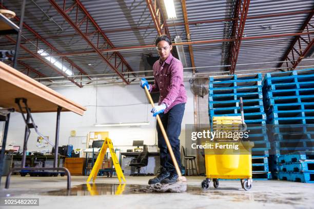 een werknemer in een magazijn schoonmaak-up een gevaar van gemorste vloeistof. - opgepast-gladde-vloer stockfoto's en -beelden