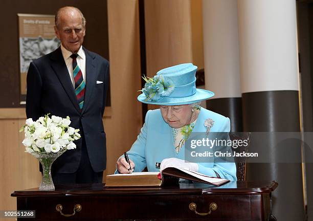 Queen Elizabeth II signs the visitors book as Prince Philip, Duke of Edinburgh looks on during a visit to the Canadian Museum of Nature on June 30,...