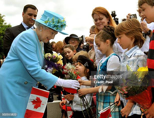 Queen Elizabeth II is given flowers by children after unveiling a statue of Oscar Peterson the legendary Canadian jazz pianist on June 30, 2010 in...