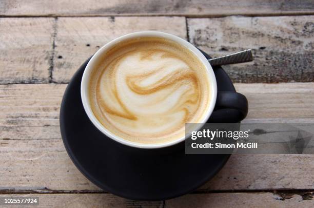 flat white coffee in a black cup and saucer on a wooden cafe table - coffee foam imagens e fotografias de stock
