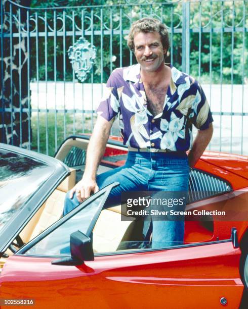 Tom Selleck as the titular investigator in the television series 'Magnum, P.I.', circa 1985. He is posing with his red Ferrari 308.
