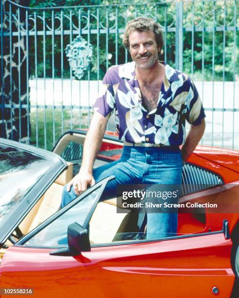 Tom Selleck as the titular investigator in the television series 'Magnum, P.I.', circa 1985. He is posing with his red Ferrari 308.