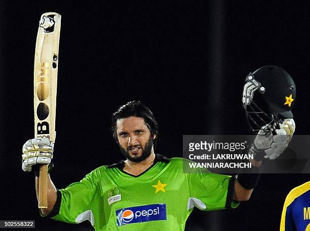 Pakistan cricket captain Shahid Afridi raises his bat and helmet in celebration after scoring a century during the first One Day International...