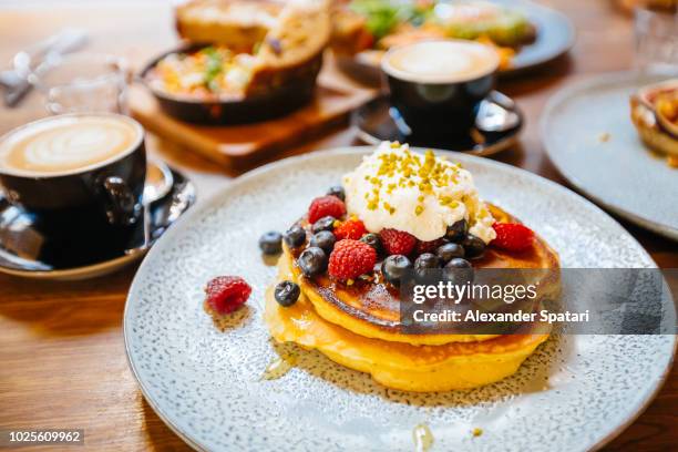 stack of pancakes with fresh blueberry, raspberry and ricotta cheese on a plate, served with coffee in cafe - new york food stockfoto's en -beelden