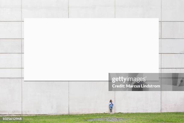 woman standing by a large blank billboard - billboard wall stock pictures, royalty-free photos & images