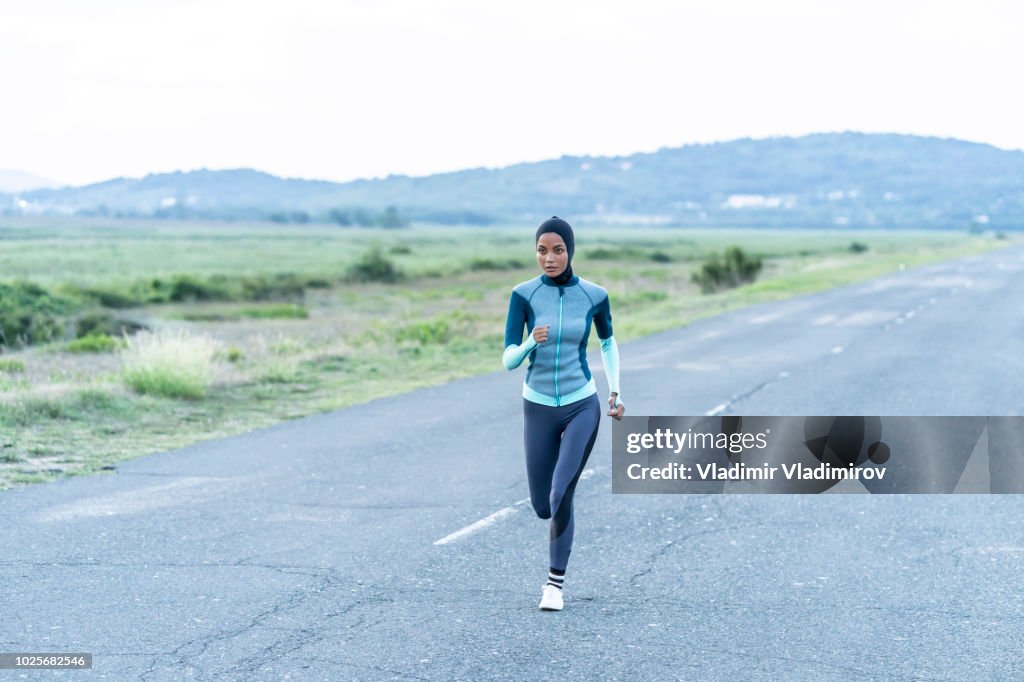 Sportswoman with hijab jogging on road near the sea