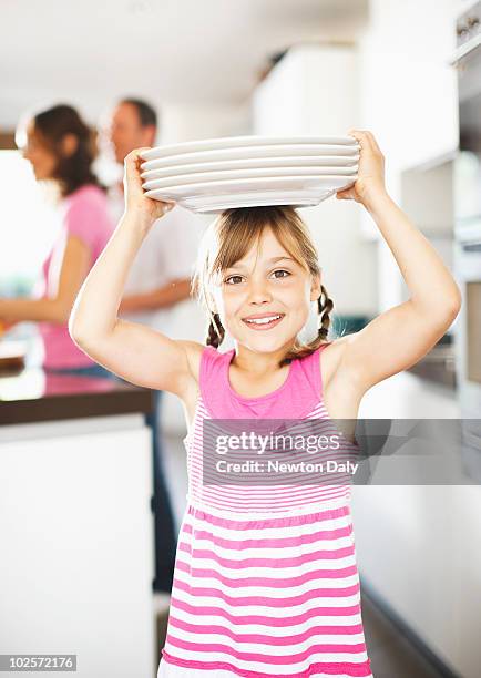 girl (8-9) balancing plates on her head , smiling - portare sulla testa foto e immagini stock