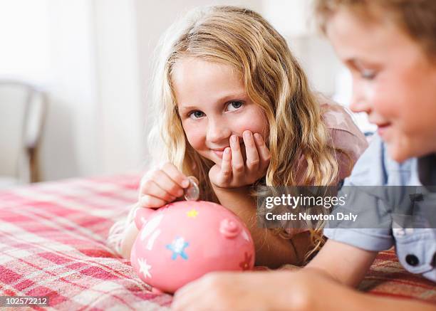 boy and girl putting coin in piggy bank - blonde girl piggy bank stock-fotos und bilder