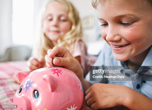 boy and girl putting coin in piggy bank - blonde girl piggy bank stock-fotos und bilder