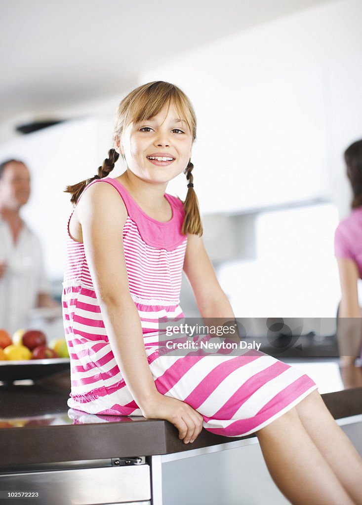 Girl (8-9) sitting in kitchen, smiling