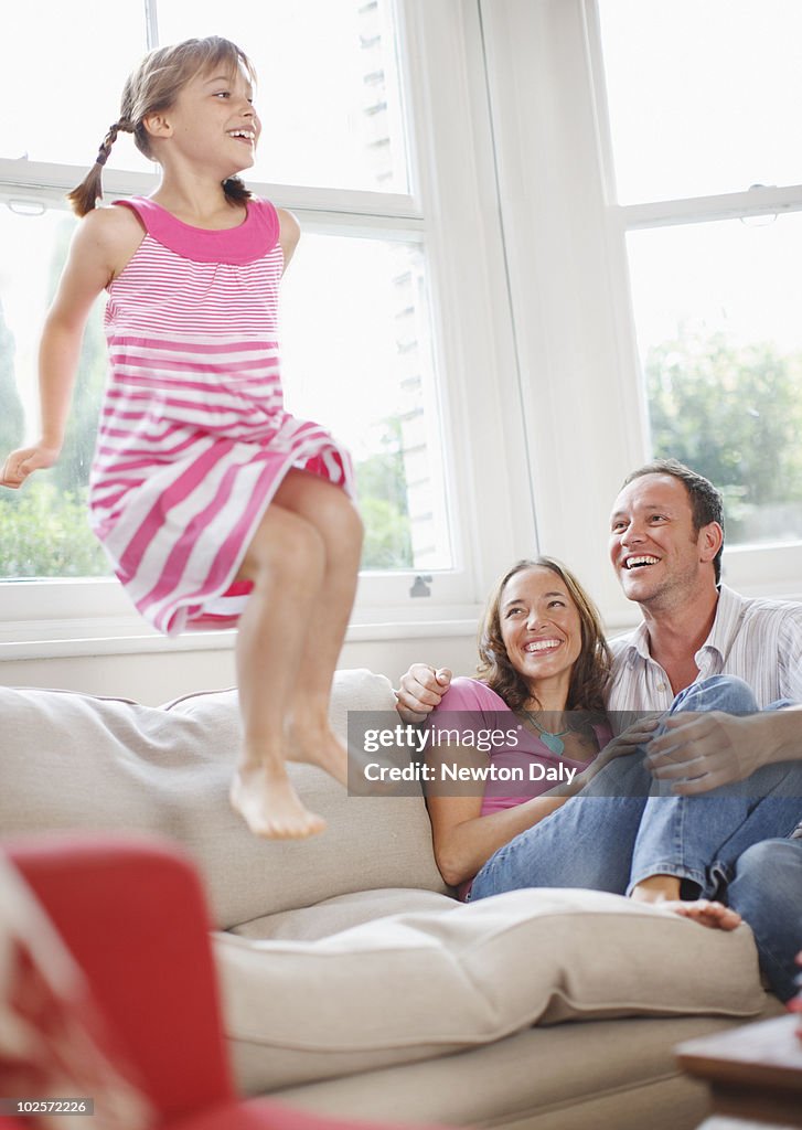 Daughter jumping on sofa with parents beside her