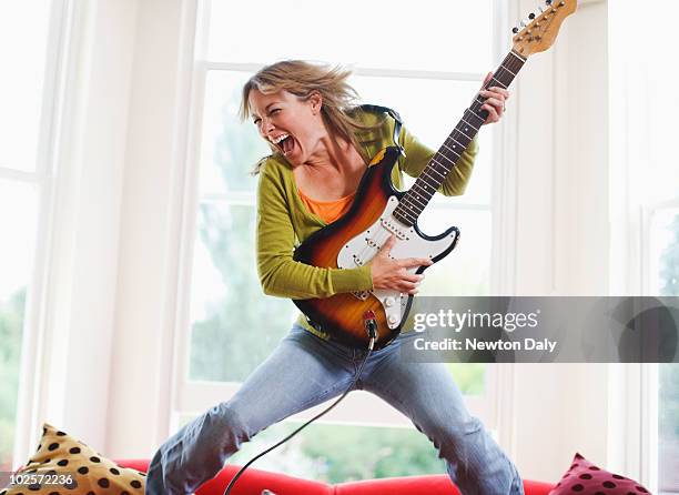 woman playing electric guitar in sitting room - electric guitar foto e immagini stock