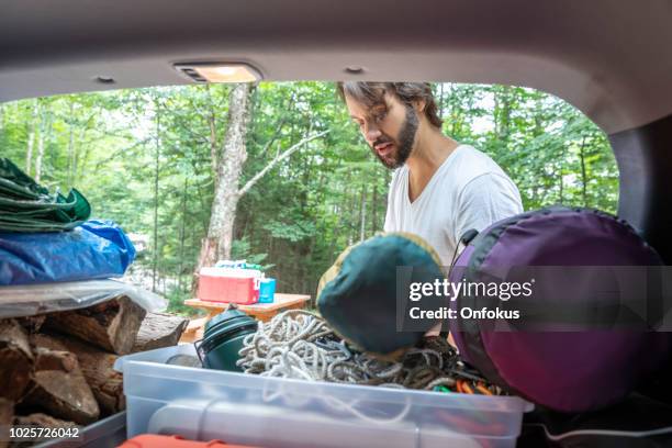 man unloading the car trunk packed with luggage and other items for road trip and camping - car camping luggage stock pictures, royalty-free photos & images