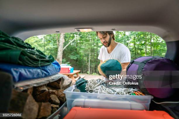 man unloading the car trunk packed with luggage and other items for road trip and camping - car camping luggage stock pictures, royalty-free photos & images