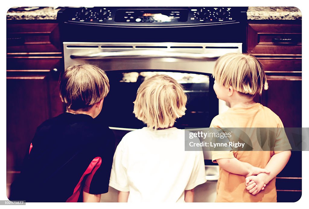 Three kids watching cookies bake