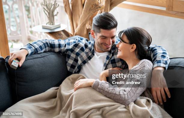 liebespaar vor dem fernseher in ihrer winter-hütte auf dem sofa liegend - warm kalt stock-fotos und bilder