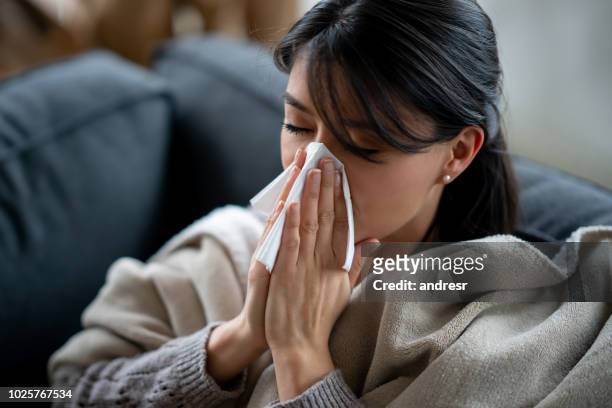 donna malata a casa che soffia il naso con un fazzoletto - closeup of a hispanic woman sneezing foto e immagini stock