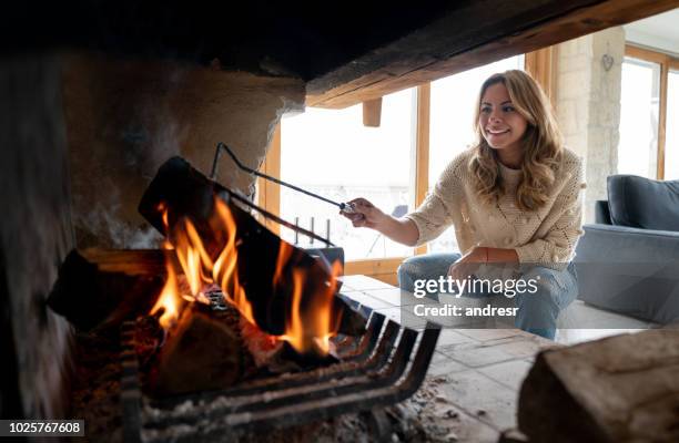 mujer en un albergue de invierno quemando troncos y mirando feliz - chimney fotografías e imágenes de stock