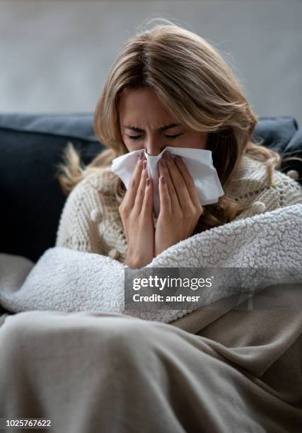 donna malata a casa che soffia il naso con un fazzoletto - closeup of a hispanic woman sneezing foto e immagini stock
