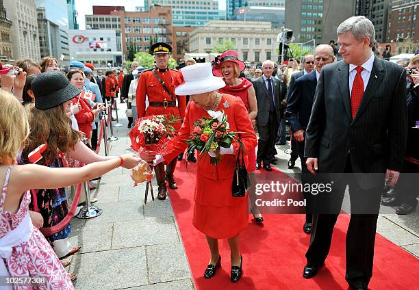 Queen Elizabeth II is given flowers by girls, as Canadian Prime Minister Stephen Harper watches, after arriving to attend the Canada Day celebrations...