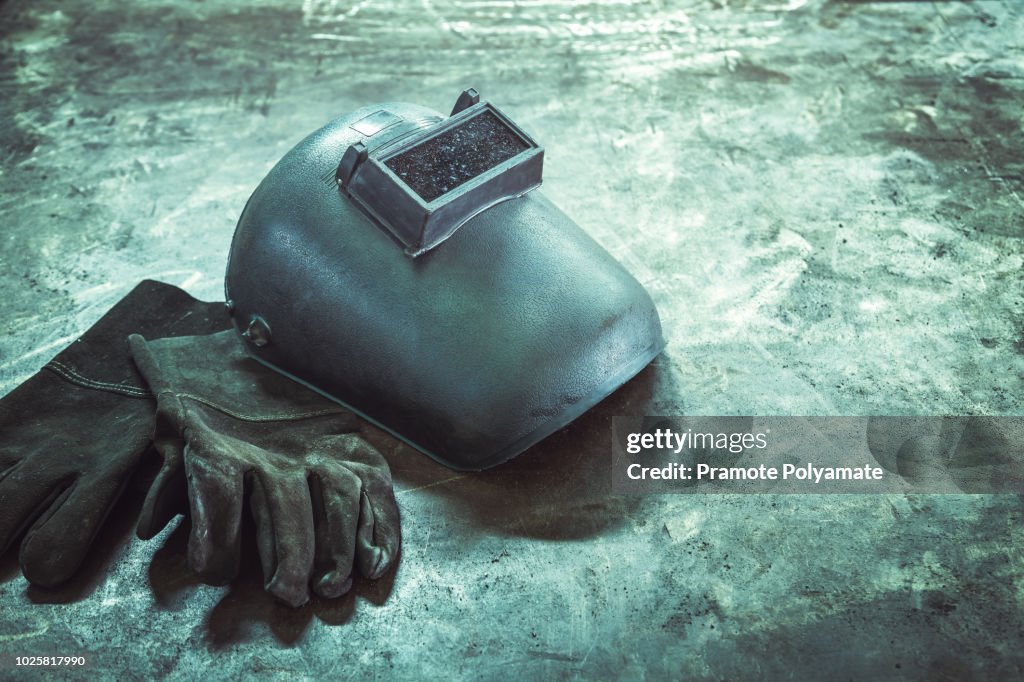 Inverted welding machine welding equipment on a wooden desk with welding mask, leather gloves, accessories for arc welding.