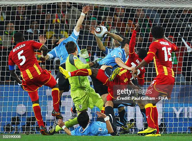 Dominic Adiyiah of Ghana heads the ball towards goal and Luis Suarez of Uruguay handles the ball off the line during the 2010 FIFA World Cup South...