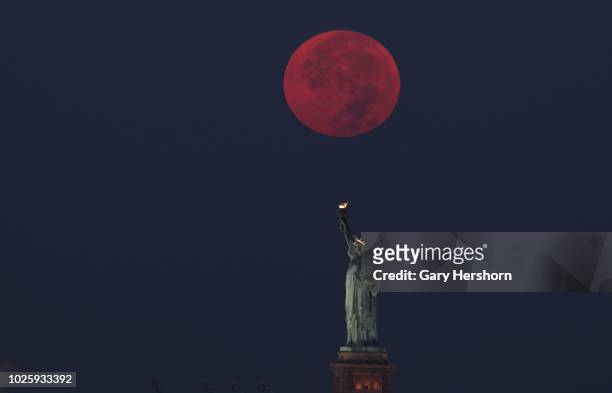 The full sturgeon moon sets behind the Statue of Liberty at sunrise on August 26, 2018 in New York City.