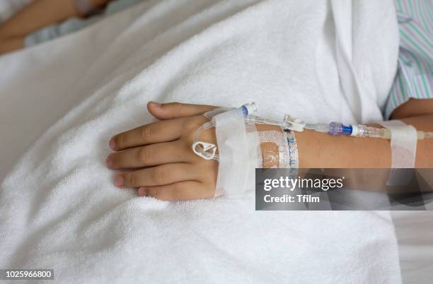 close up on young asian boy hand of a patient with medical drip or iv drip in hospital ward, selective focus. - iv pump stock pictures, royalty-free photos & images