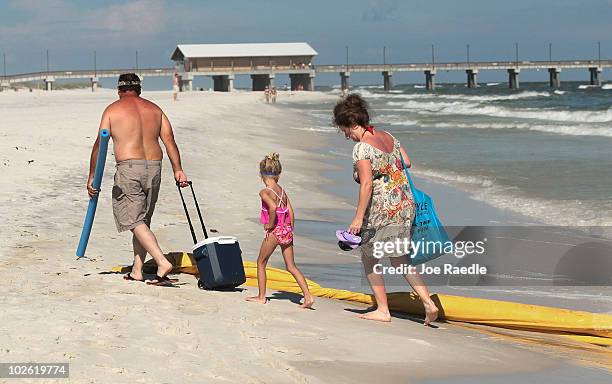 People walk around an oil containment boom that had washed ashore as they walk along a beach which was not as busy as last year as people stayed away...