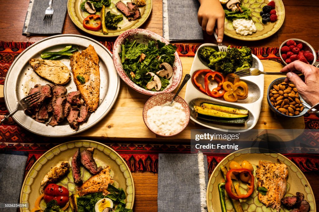 A ketogenic meal laid out on a dining table with the hands of people serving themselves
