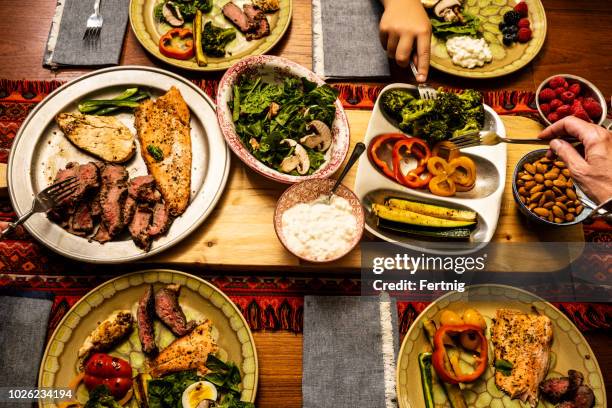 a ketogenic meal laid out on a dining table with the hands of people serving themselves - ketogenic diet stock pictures, royalty-free photos & images