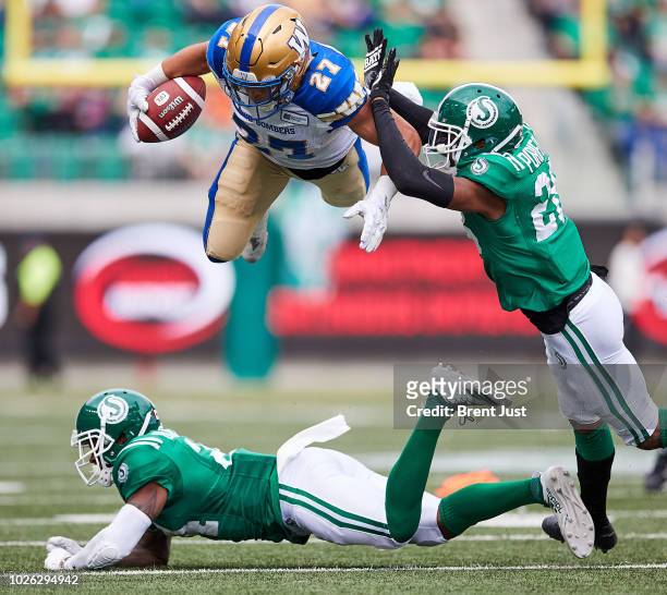Kienan LaFrance of the Winnipeg Blue Bombers leaps over a diving Will Blackmon of the Saskatchewan Roughriders in the game between the Winnipeg Blue...