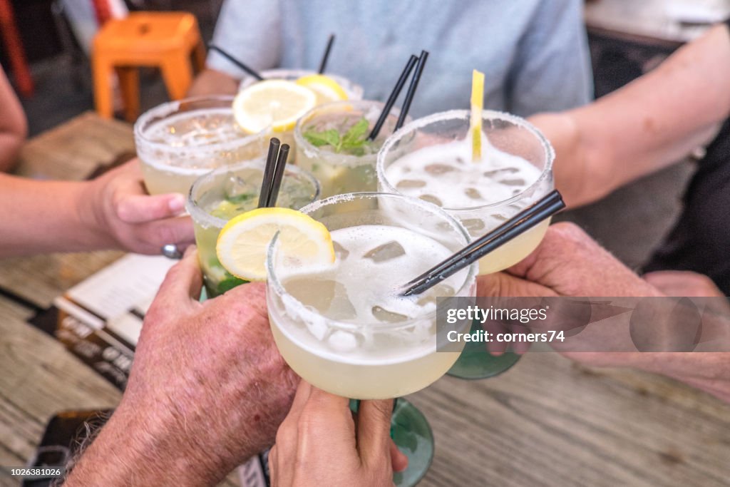 Hands young and old celebrating making a toast and clinking cocktail glasses with margaritas and mojito drinks at celebration