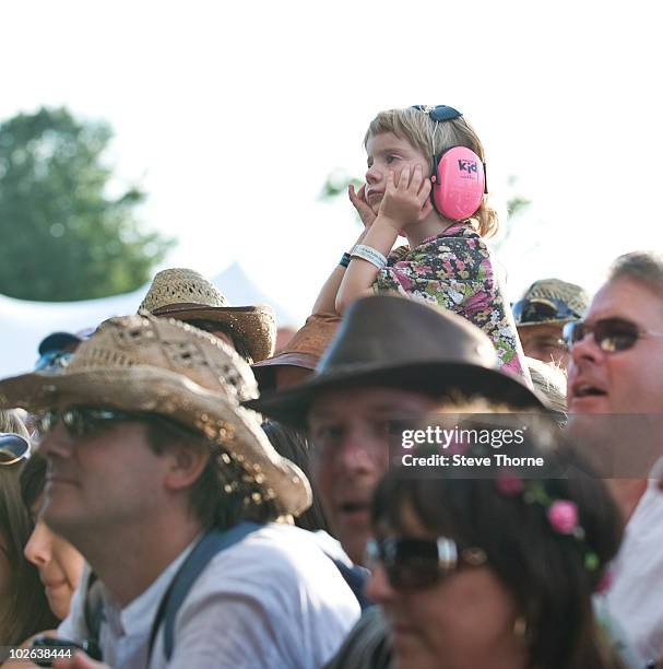 Child wearing ear defender headphones sitting on shoulders in the crowd and looking bored during the first day of Cornbury Festival at Cornbury Park...