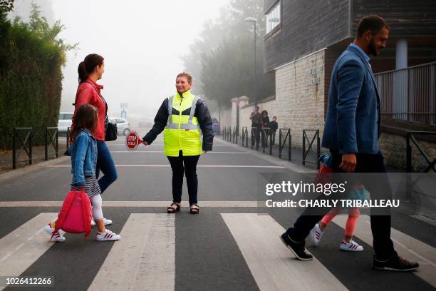 An employee of the city hall helps children to cross the street as they walk toward their school on September 3, 2018 in Caen, northwestern France,...