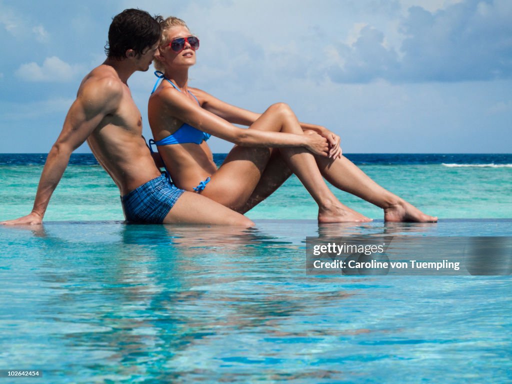 Young couple relaxing on edge of infinity pool