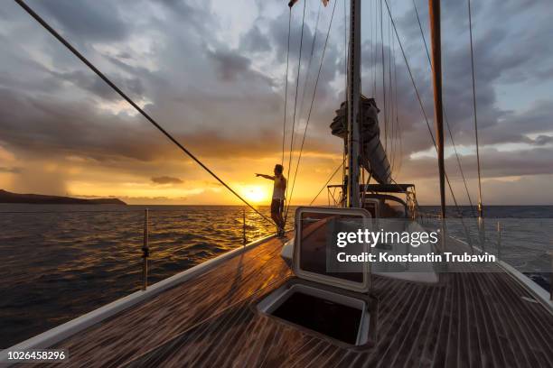 man on deck of large yacht pointing at sunset on horizon, lombok, indonesia - sailboat silhouette stock pictures, royalty-free photos & images