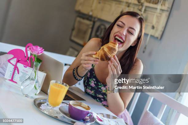 frau isst genüsslich ein croissant und lacht - frau essen stock pictures, royalty-free photos & images