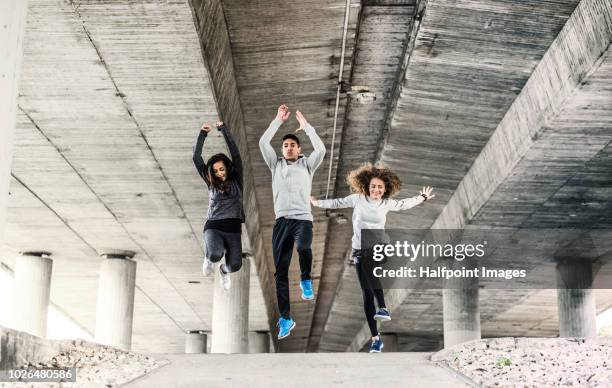 a group of young sporty friends jumping outside under the bridge in the city, doing exercise. - gray shoe stock-fotos und bilder