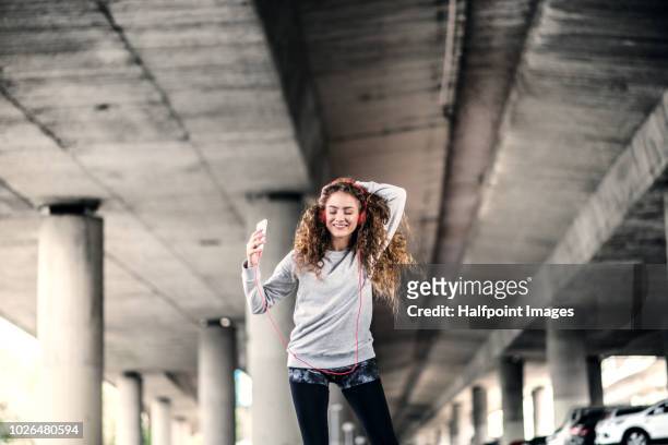 a beautiful young woman with smartphone and red headphones under the bridge in the city, listening to music. - musica y verano fotografías e imágenes de stock