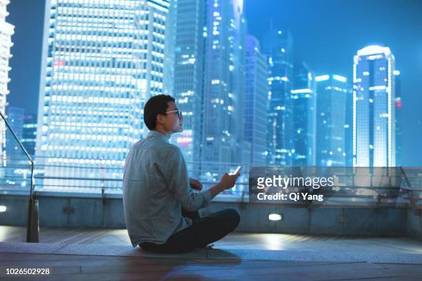 young businessman looking at smartphone on the roof - sitting on a cloud stock pictures, royalty-free photos & images