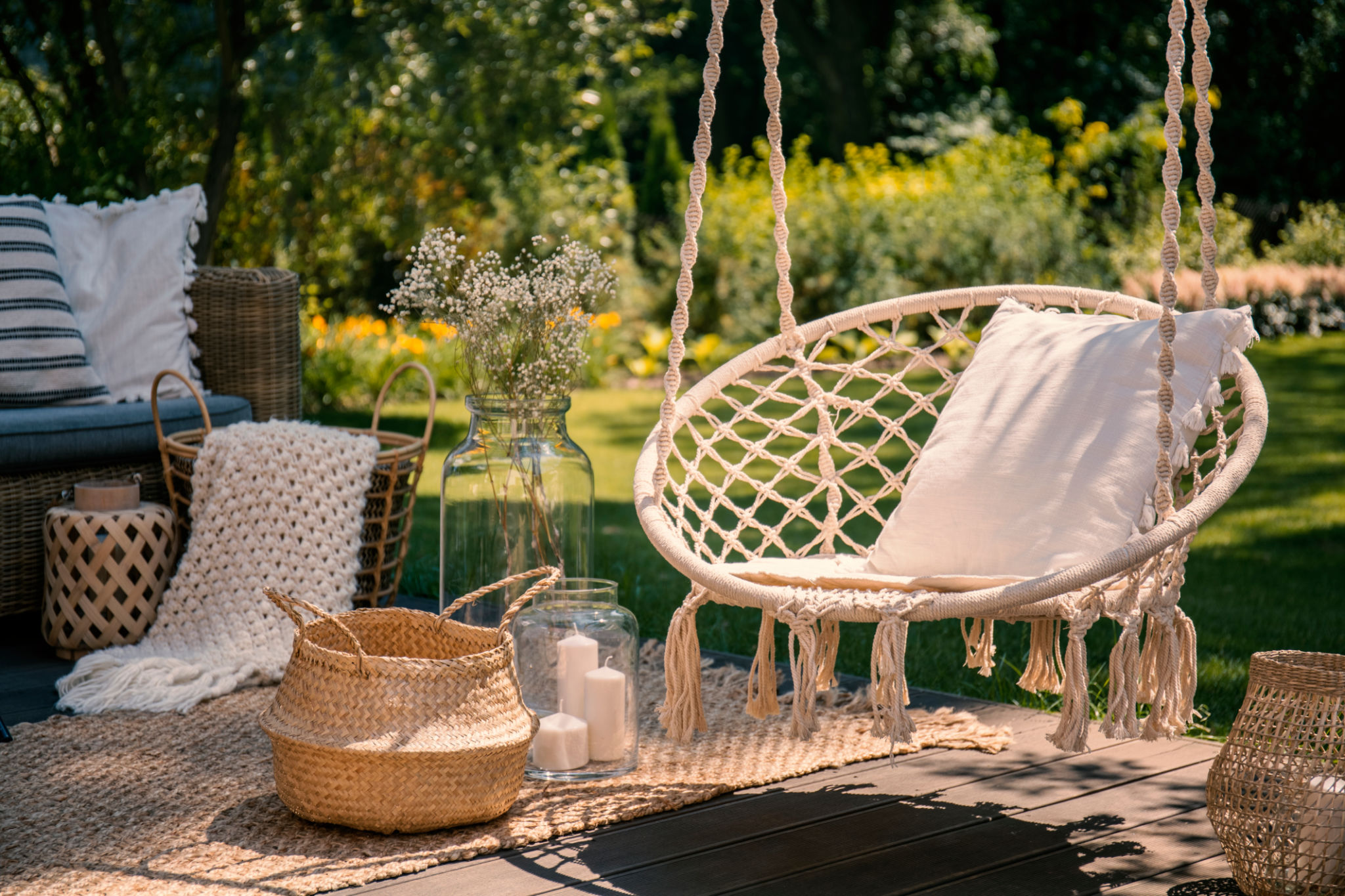 A beige string swing with a pillow on a patio. Wicker baskets, a rug and a blanket on a wooden deck in the garden. A beige string swing with a pillow on a patio. Wicker baskets, a rug and a blanket on a wooden deck in the garden.