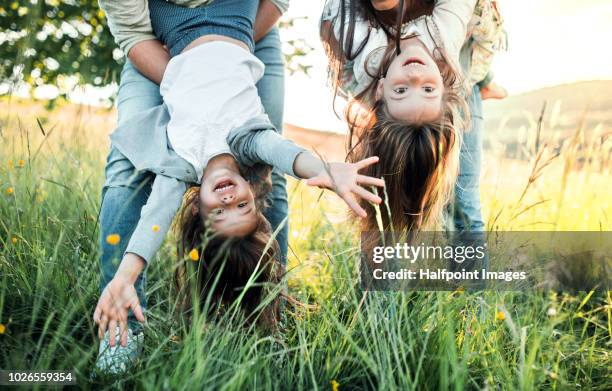 a father and mother holding their daughters upside down outside in spring nature. - happy family imagens e fotografias de stock