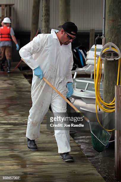 Worker uses a net to scoop small globs of oil from the water off of Rigolets Harbor restaurant and lounge as some of the oil residue washes in from...