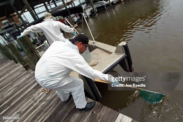 Workers use nets to scoop small globs of oil from the water off of Rigolets Harbor restaurant and lounge as oil residue washes in from the Deepwater...